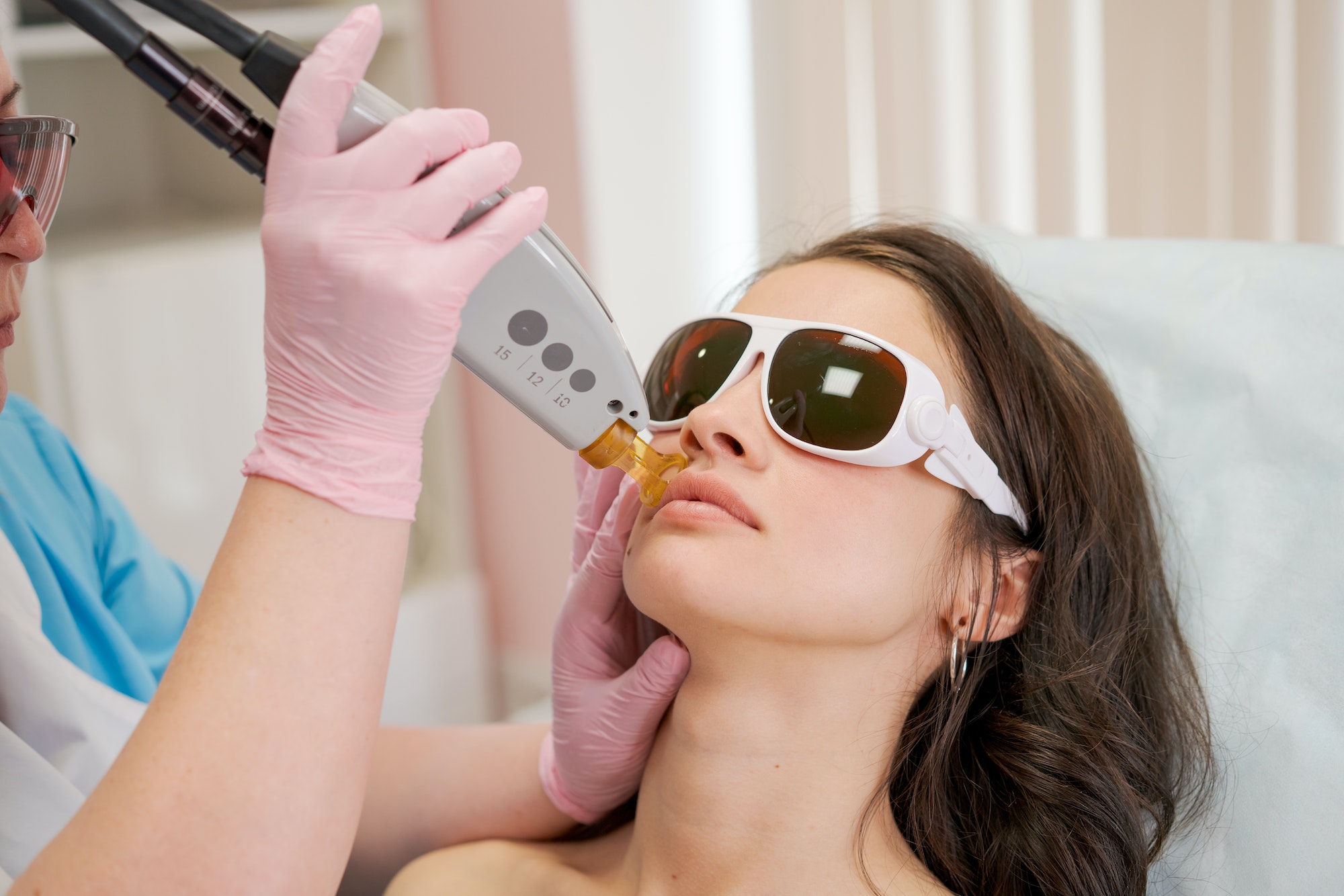 Therapist cosmetologist makes laser treatment for woman's face in SPA beauty